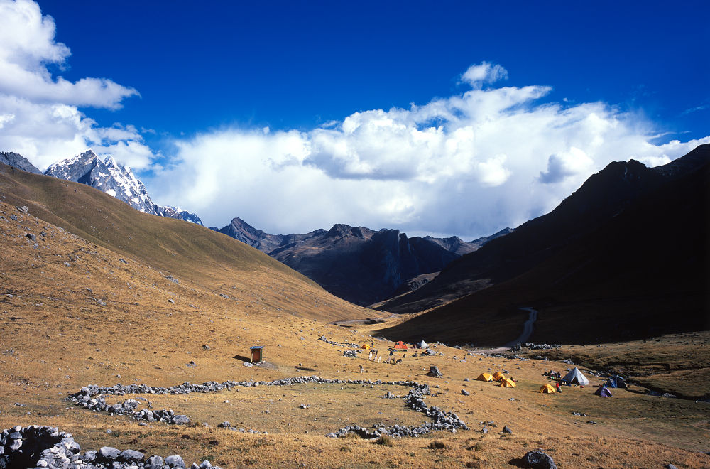 Notre premier campement (premier plan) au départ de notre trek se trouve à Matacancha ; les tentes jaunes sont les nôtres, la grande grise sert de réfectoire et de lieu couchage pour les muletiers, la bleue, sert de cuisine et de lieu de couchage pour le cuisinier et deux autres servant aux guides. Nous partageons le campement avec un autre groupe car les emplacements sont définis. La Cordillère Huayhuash est gérée par les communautés qui y habitent en percevant une taxe au passage des portes marquant l'entrée dans la communauté et la Cordillère ; cette taxe servira à entretenir les campements.<br />Prise de vue : 14/07/08, 15h55