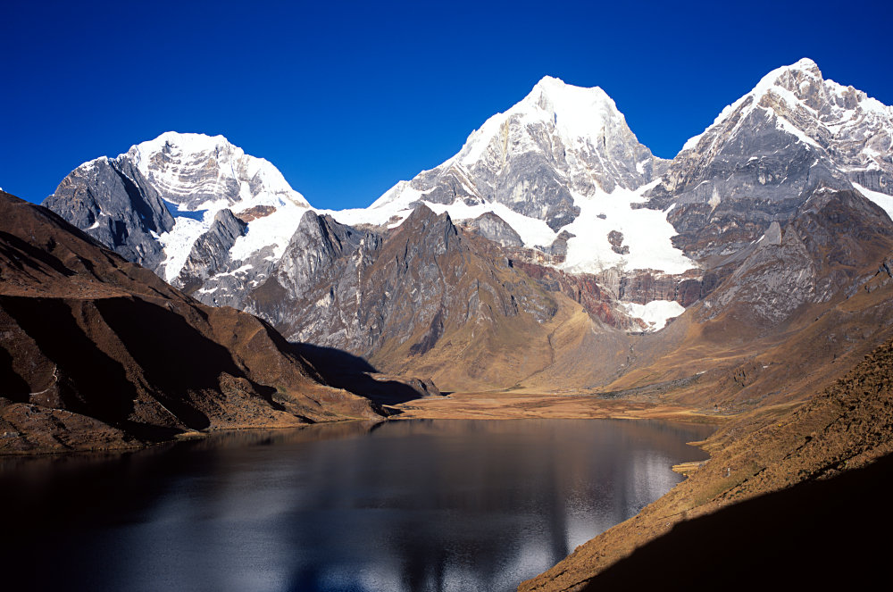 Depuis notre campement, le soleil illumine le spectacle de ces 3 seigneurs : Siula Grande (6344 m), Yerupaja (6617 m) et Yerupaja Chico (6089 m) qui se reflètent dans la Laguna Carhuacocha (4138 m).<br />Prise de vue : 17/07/08, 07h10